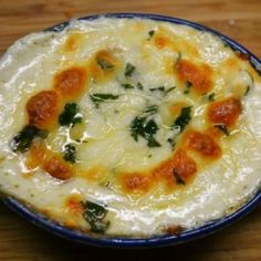 a blue bowl filled with cheese and spinach covered in sauce on top of a wooden table