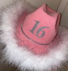 a pink hat with the number 16 on it and white fur around it, sitting on a table