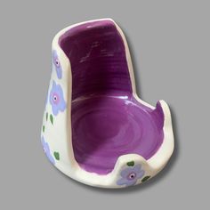 a purple and white bowl with flowers painted on the bottom, sitting in front of a gray background