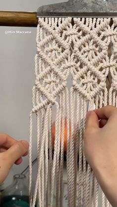 two hands are working on an object with white yarn and wood dows in the background