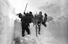 several men are standing in the snow with their bikes