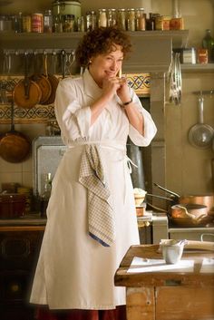 a woman is standing in the kitchen with her hand on her chin and looking at something