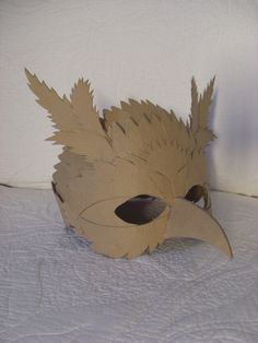 a mask made out of cardboard with leaves on the face and nose, sitting on a bed