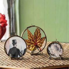 three miniature pictures of people and a leaf on a wicker table with a red vase in the background