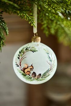 a glass ornament hanging from a christmas tree with pine cones and acorns