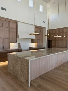 a large kitchen with wooden cabinets and marble counter tops, along with pendant lights hanging from the ceiling