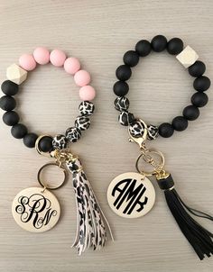 two bracelets with monogrammed charms and tassels are on a table