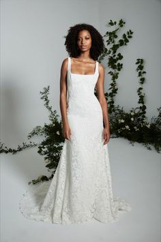 a woman in a white wedding dress posing for the camera with greenery behind her