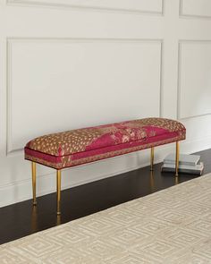 a red bench sitting on top of a wooden floor next to a white wall and rug