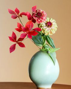 a green vase filled with flowers on top of a wooden table