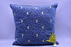 a blue pillow with yellow stars and the moon on it is sitting next to a plant