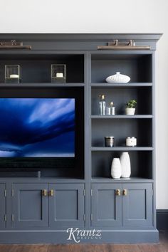 an entertainment center with gray painted cabinets and white vases