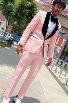 a man in a pink suit and white shoes standing on the sidewalk with his hands in his pockets