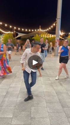 a group of people are dancing around in the street at night with lights strung overhead