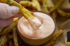 a person dipping some kind of food into a small bowl filled with sauce and fries