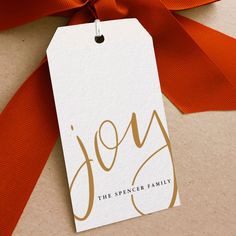 a gift tag with the word joy on it is tied to a red satin ribbon