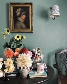 a table topped with flowers next to a painting and a vase filled with daisies