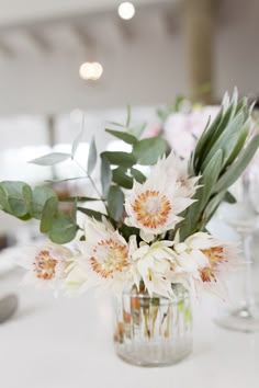 a vase filled with lots of flowers on top of a white table covered in greenery