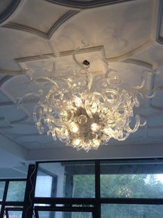 a chandelier hanging from the ceiling in a room with large windows and glass doors