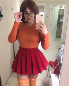 a woman taking a selfie in front of a mirror wearing glasses and a red skirt