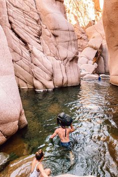 two people are wading in the water near large rocks