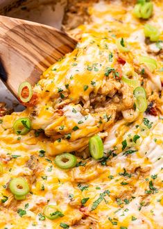 a casserole dish with meat, cheese and green onions on it is being lifted by a wooden spatula