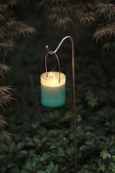 a lit candle sitting on top of a metal stand in the middle of some bushes