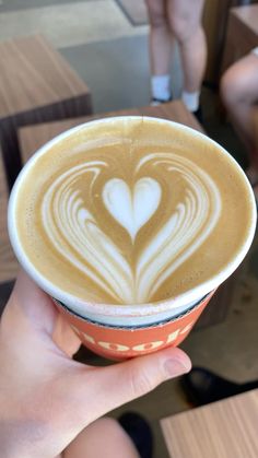 a person holding up a cup with a heart drawn on it in front of other people