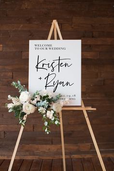 a sign that says welcome to our wedding on top of a wooden easel with flowers