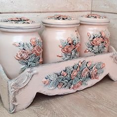 three pink vases sitting on top of a wooden shelf with flowers painted on them