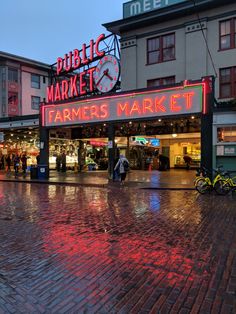 people walking in front of a farmers market on a rainy day with red and green lights