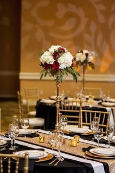 the table is set with black linens, gold chargers and white flowers in tall vases