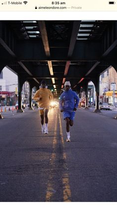 two men running under an overpass in the city at night, one is wearing blue and the other is yellow