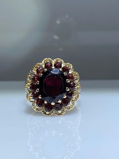 14K yellow gold ring with genuine garnets. This gorgeous statement ring has one of the most vibrant garnets I've seen! It turns to a bright wine color in the sunlight! The large oval garnet weighs about 4.00 carats. It does have some small scratches on the table but they are in no way distracting and are almost invisible in the sunlight. There is a garnet halo that delicately hugs the large center. The perimeter of the ring is laid with delicate roped gold. The under-basket is nice and opened to Opal Ring Vintage, Fantasy Ring, Gold Statement Ring, Garnet Jewelry, Ruby Jewelry, Wine Color, Bling Rings, Pretty Rings, Garnet Rings