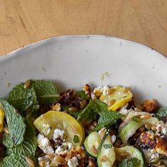 a white bowl filled with vegetables and nuts on top of a wooden table next to a fork