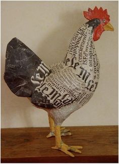 a chicken made out of newspaper sitting on top of a wooden table next to a wall