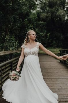 a bride and groom walking across a bridge holding hands