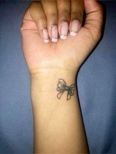 a woman's wrist with a small bow tattoo on the left side of her arm