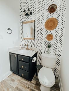 a white toilet sitting next to a sink in a bathroom under a mirror on top of a wooden floor