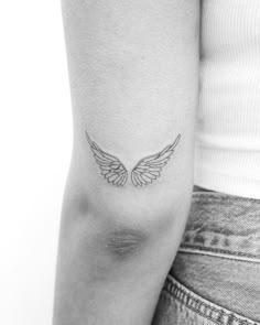 a woman's arm with an angel wing tattoo on the left side of her arm