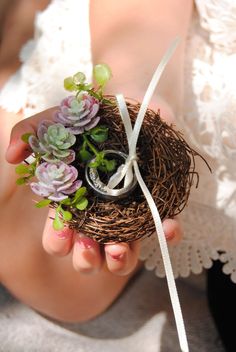 a woman holding a small bird nest with succulents and a wedding ring