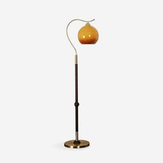 a floor lamp with an orange glass ball on the top and a brass metal base