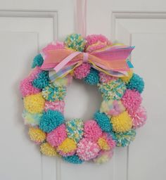 a colorful wreath hanging on a door with pink, yellow and blue pom - poms