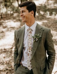 a man in a suit and tie smiles at the camera while standing in the woods