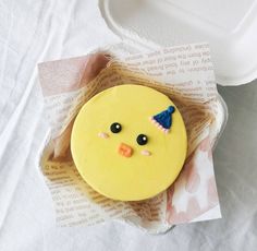 a yellow cake with a blue hat on it's head sitting in a paper wrapper