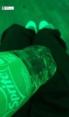 a close up of a person's feet wearing black pants and white shoes, with a green bottle in the foreground