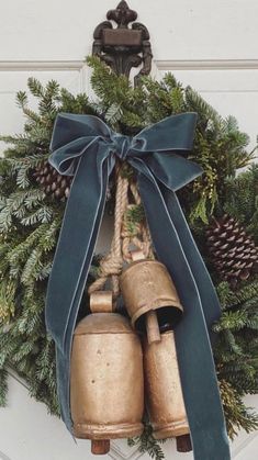 a wreath with two bells tied to it and pine cones on the door hanger