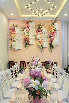 the tables are set up with white chairs and floral arrangements on the wall behind them