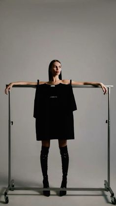 a woman in black dress and knee high boots standing next to a metal rack with her arms on it