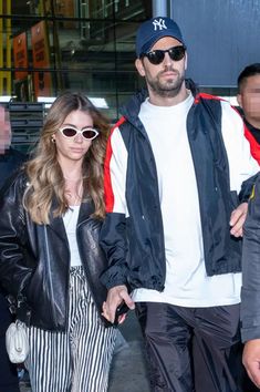 a man and woman walking down the street with sunglasses on their heads, one wearing a baseball cap